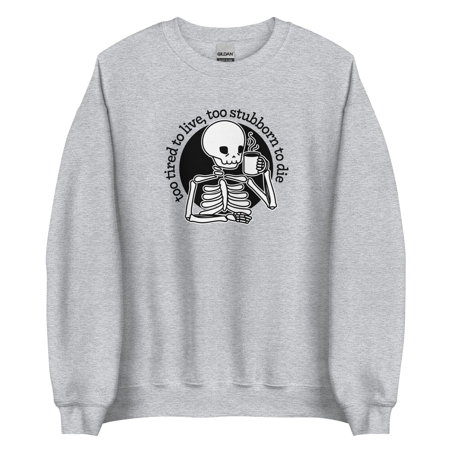 A grey crewneck sweatshirt featuring an illustration of a tired-looking skeleton holding a steaming mug. Text in an arc above the skeleton reads "too tired to live, too stubborn to die"