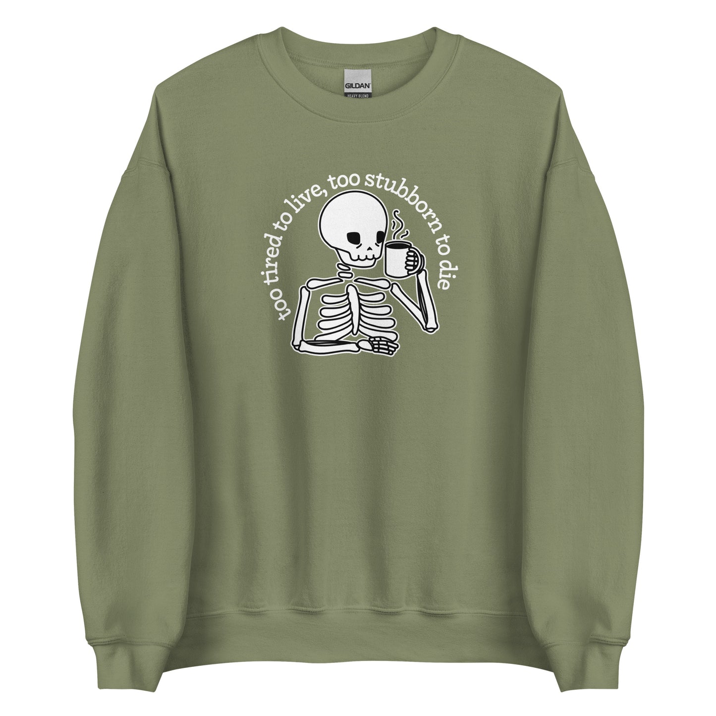 An olive green crewneck sweatshirt featuring an illustration of a tired-looking skeleton holding a steaming mug. Text in an arc above the skeleton reads "too tired to live, too stubborn to die"