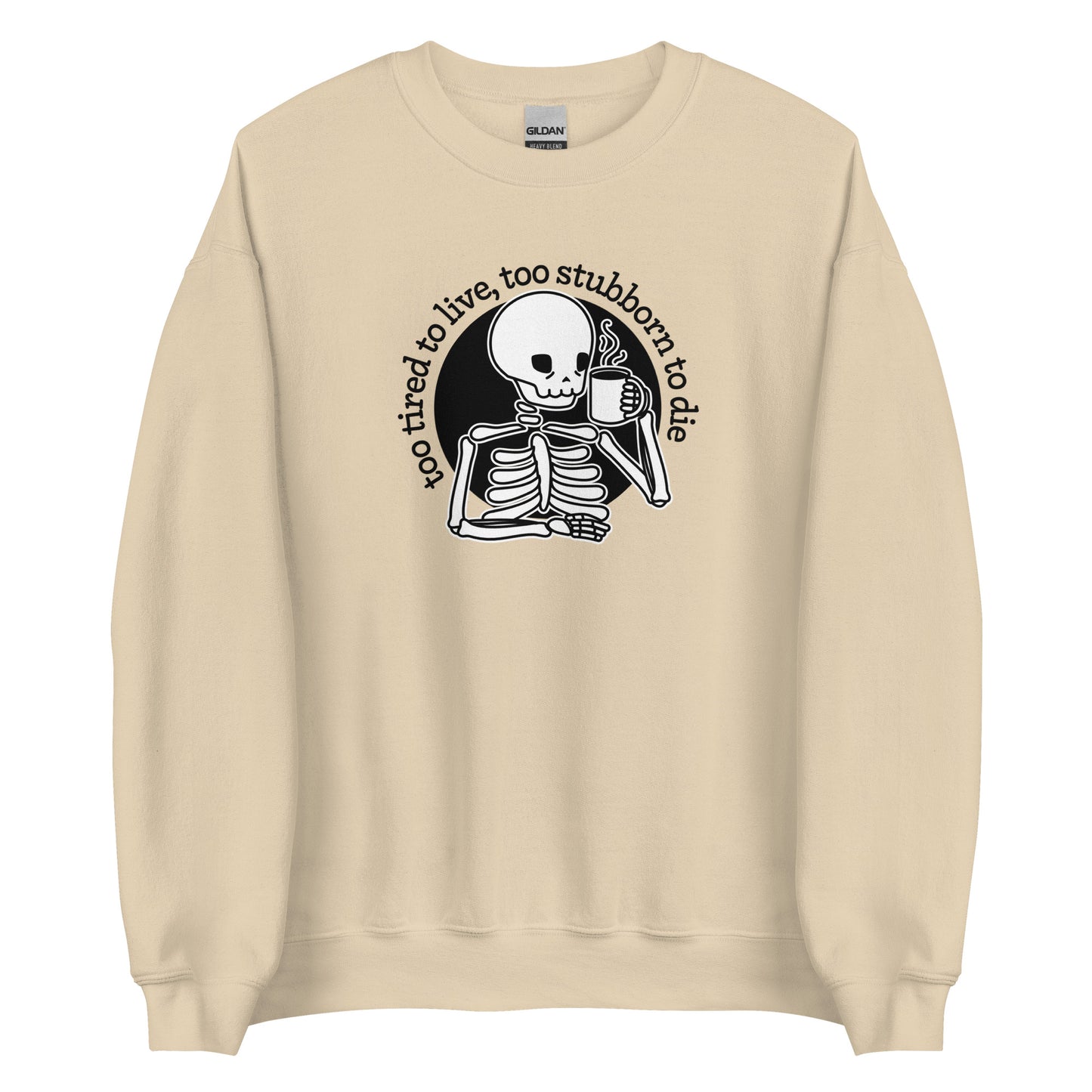 A cream-colored crewneck sweatshirt featuring an illustration of a tired-looking skeleton holding a steaming mug. Text in an arc above the skeleton reads "too tired to live, too stubborn to die"