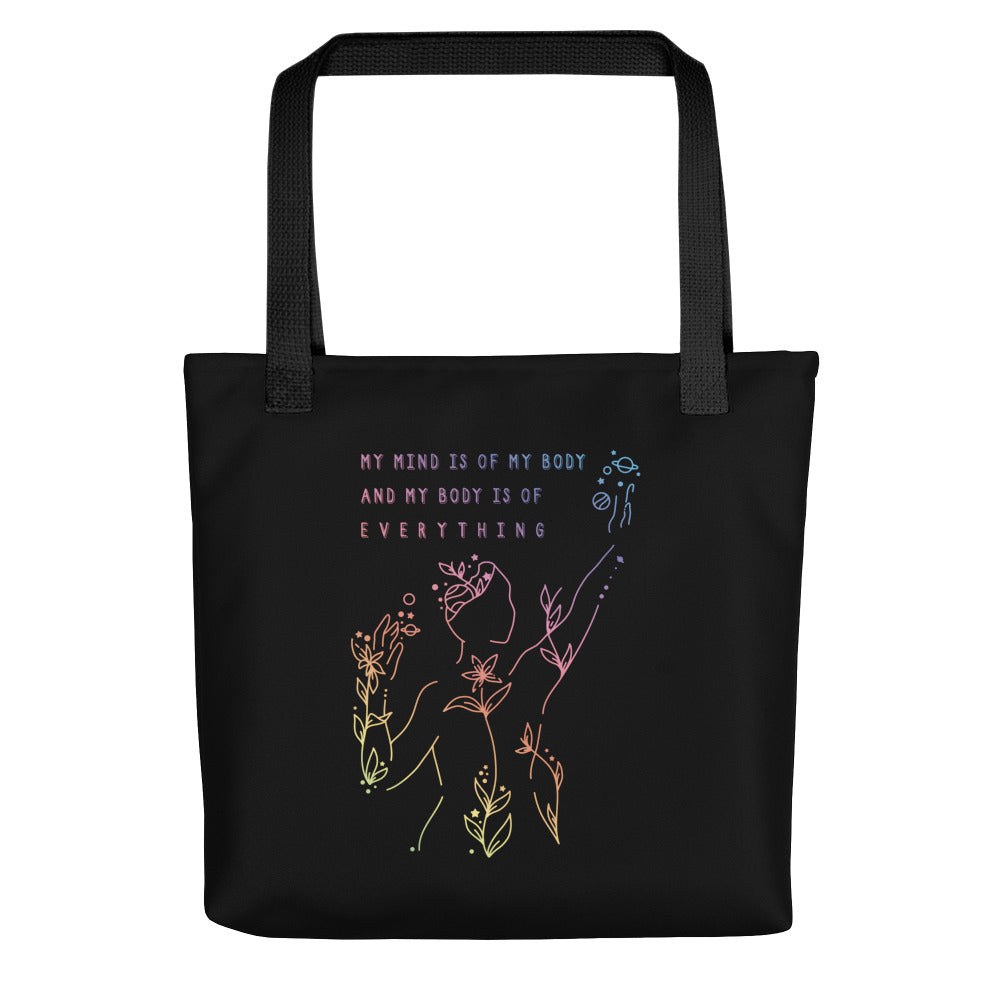 A black canvas tote bag with a black handle. The tote bag features an abstract illustration of a figure whose body is spreading out into plants and planets and stars. Text above the figure reads "My mind is of my body and my body is of everything."