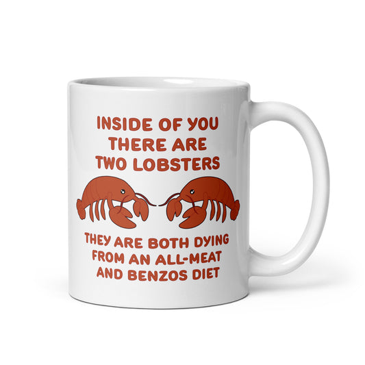 A white 11 ounce ceramic mug featuring an illustration of two lobsters. Text around the lobsters reads "Inside of you there are two lobsters." "They are both dying from an all-meat and benzos diet."