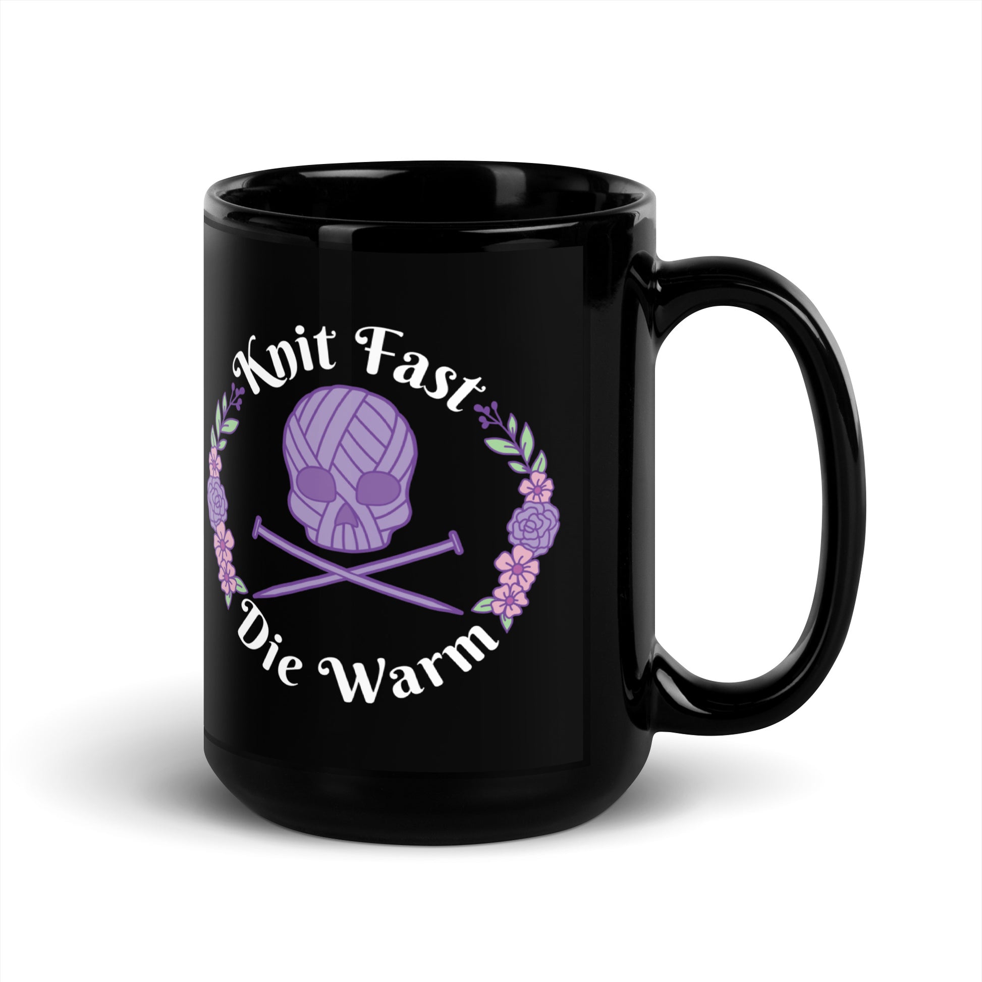 A black 15 ounce mug featuring an image of a purple skull and crossbones made of yarn and knitting needles. A floral wreath surrounds the skull, along with words that read "Knit Fast, Die Warm"
