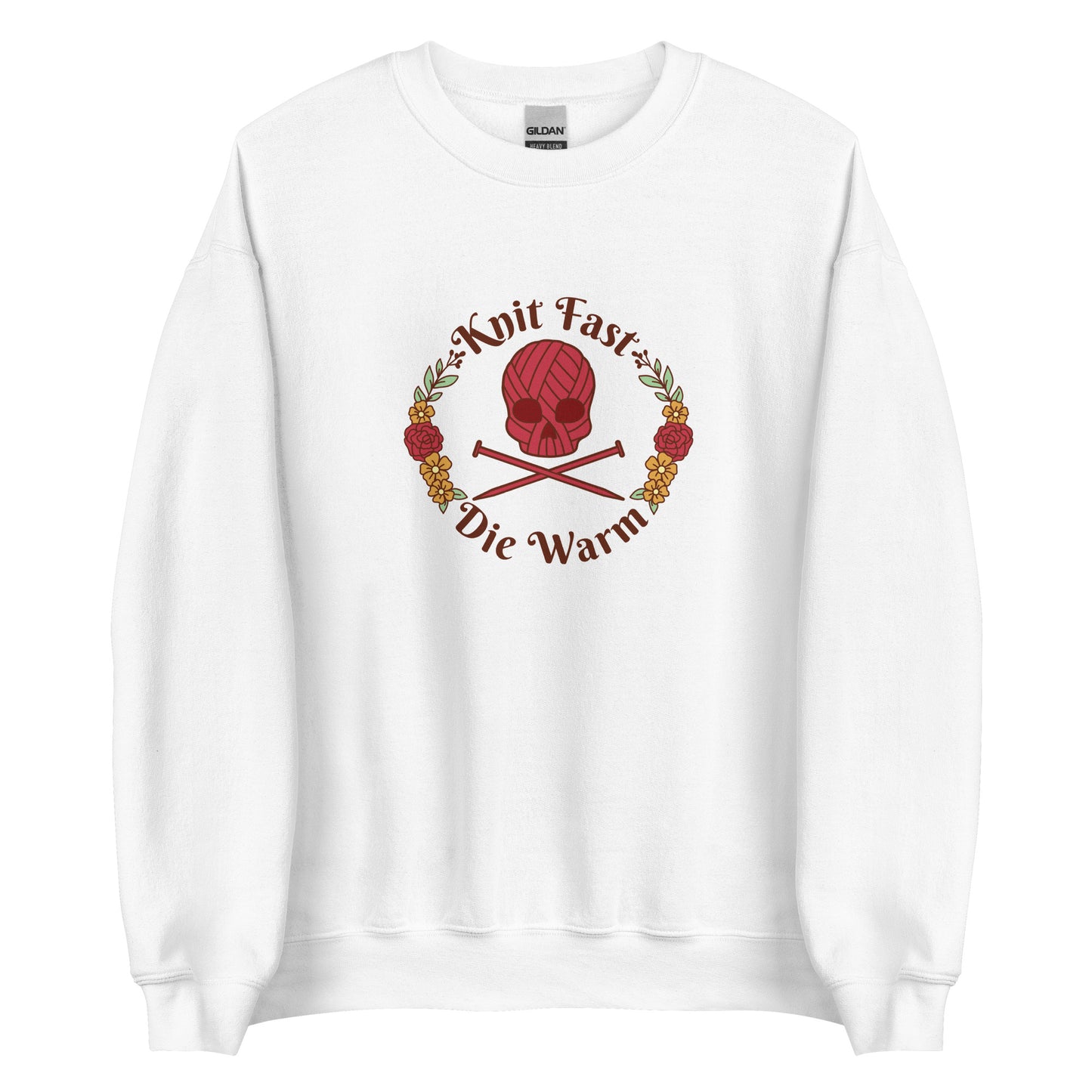 A white crewneck sweatshirt featuring an image of a skull and crossbones made of yarn and knitting needles. A floral wreath surrounds the skull, along with words that read "Knit Fast, Die Warm"
