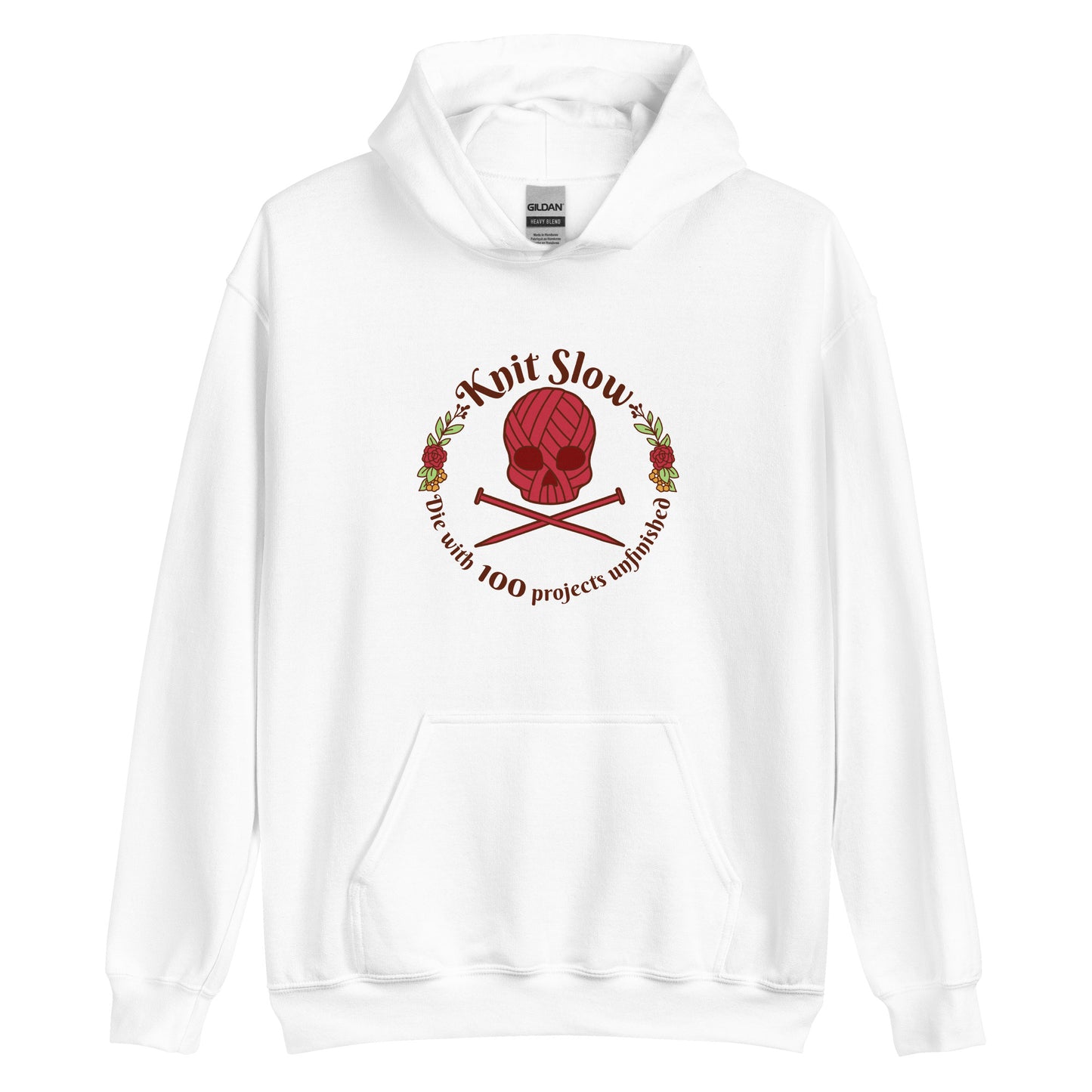 A white hooded sweatshirt featuring an image of a skull and crossbones made of yarn and knitting needles. A floral wreath surrounds the skull, along with words that read "Knit Slow, Die with 100 projects unfinished"