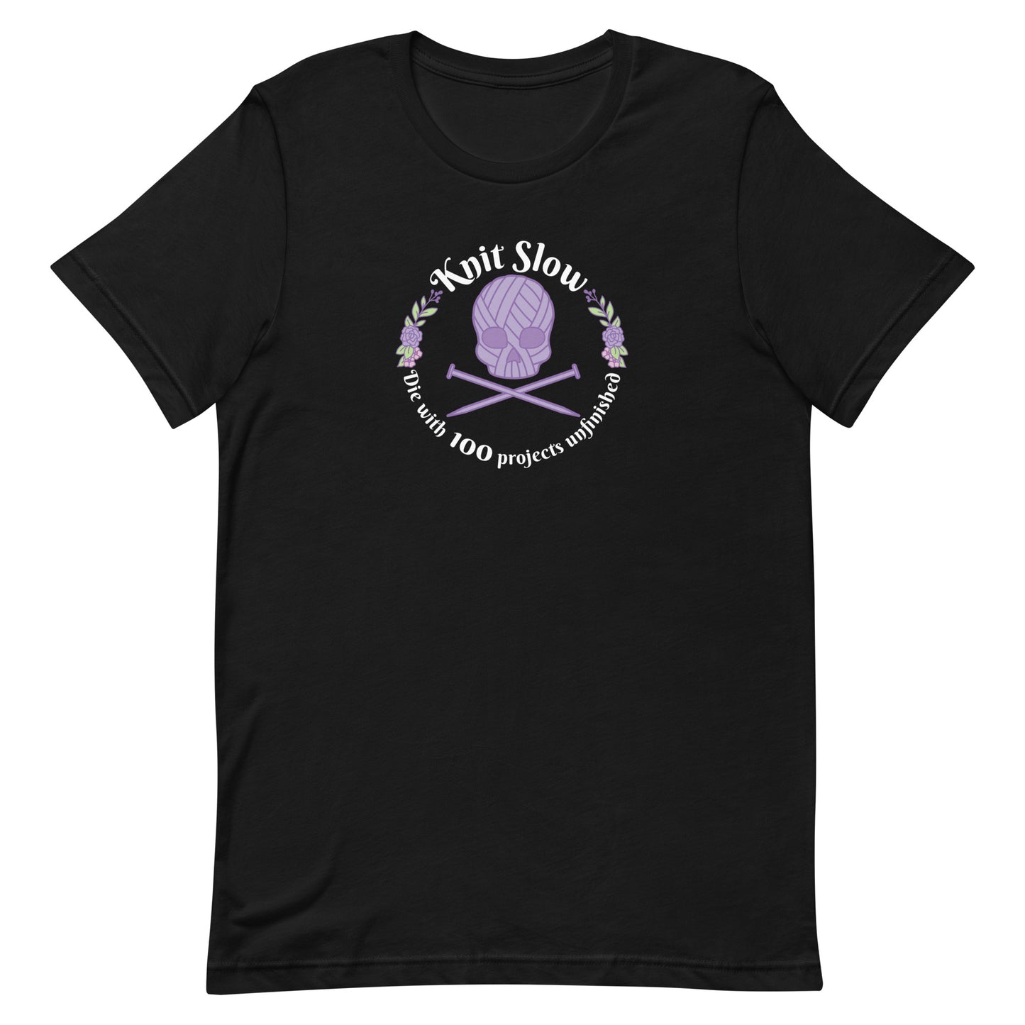 A black crewneck t-shirt featuring an image of a skull and crossbones made of yarn and knitting needles. A floral wreath surrounds the skull, along with words that read "Knit Slow, Die with 100 projects unfinished"