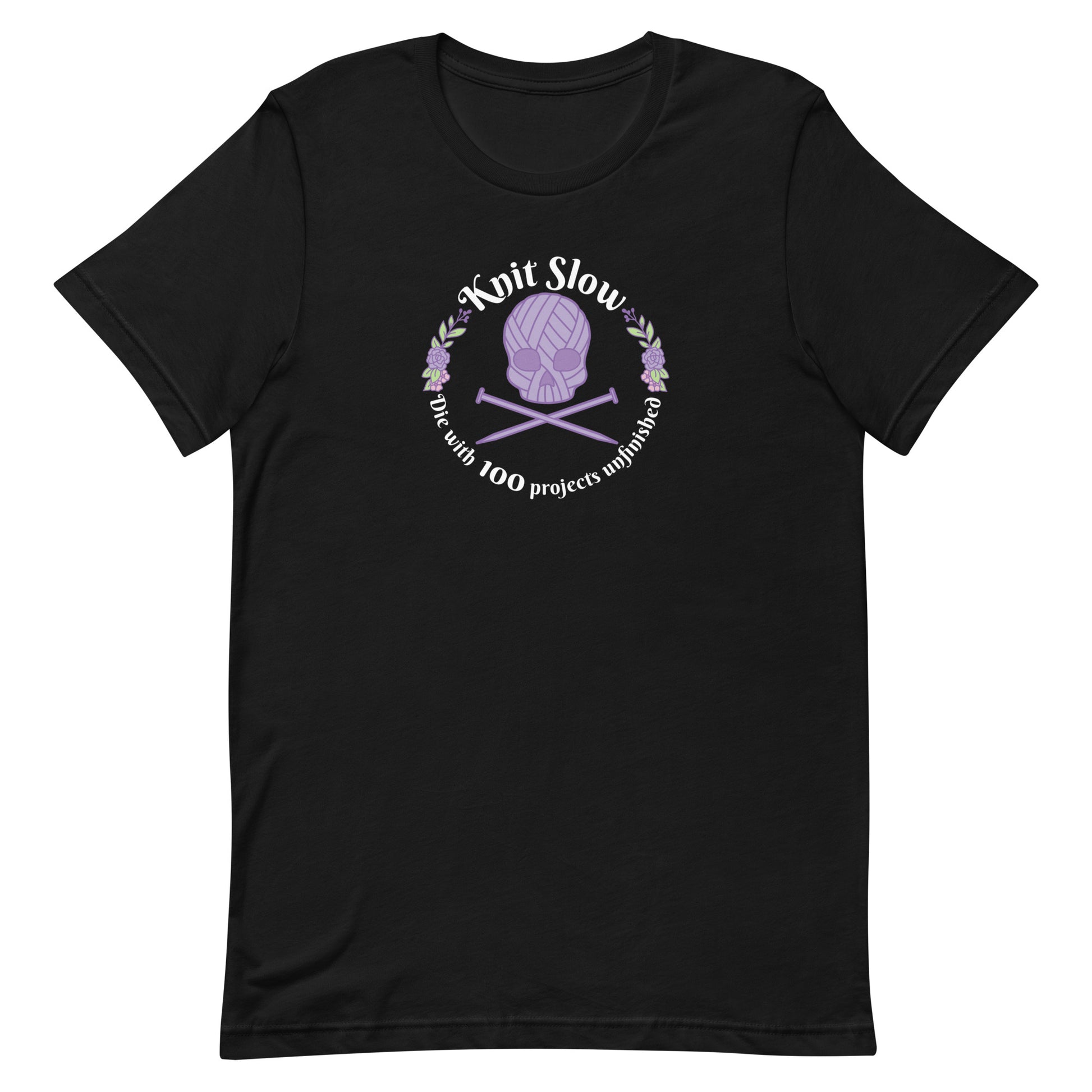 A black crewneck t-shirt featuring an image of a skull and crossbones made of yarn and knitting needles. A floral wreath surrounds the skull, along with words that read "Knit Slow, Die with 100 projects unfinished"