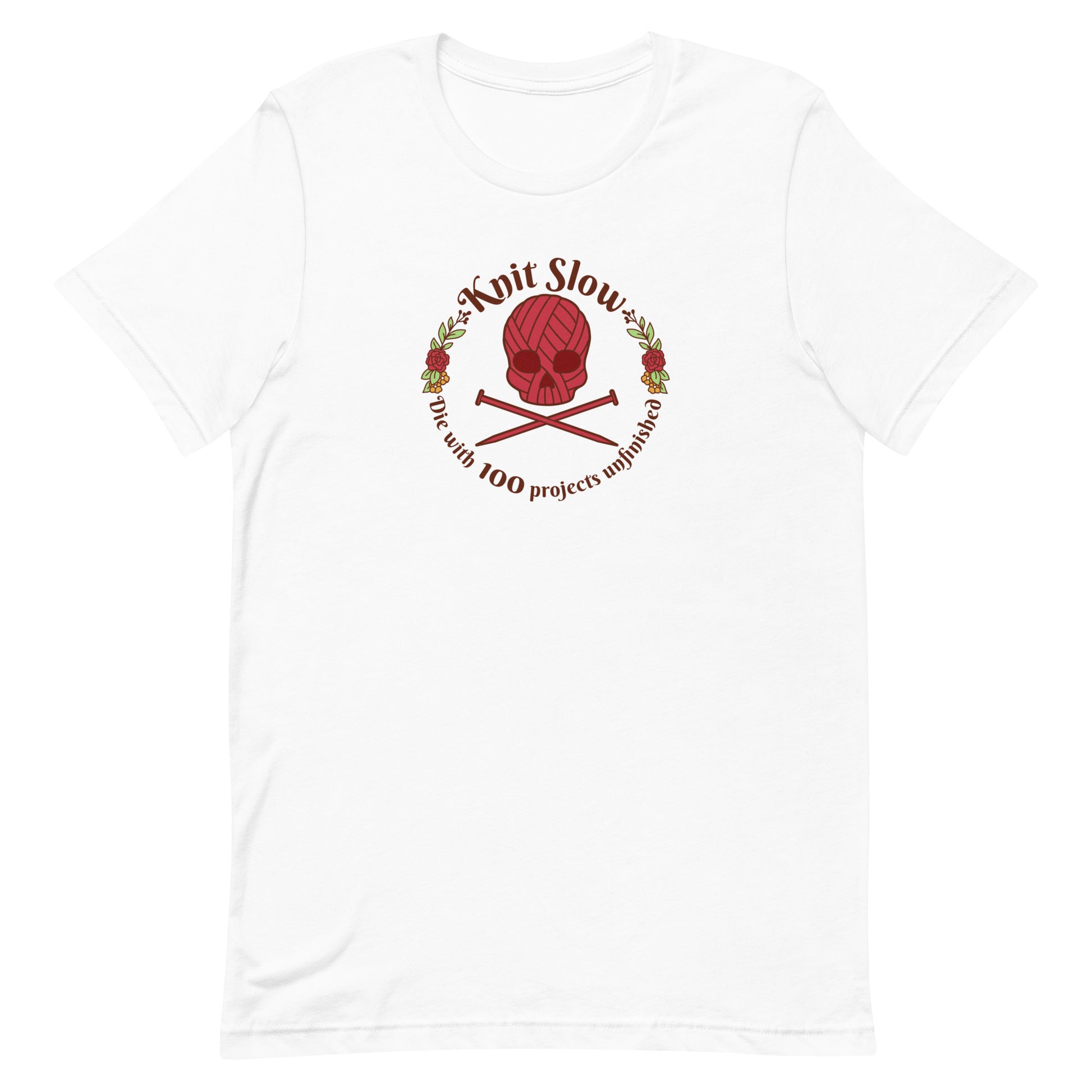 A white crewneck t-shirt featuring an image of a skull and crossbones made of yarn and knitting needles. A floral wreath surrounds the skull, along with words that read "Knit Slow, Die with 100 projects unfinished"