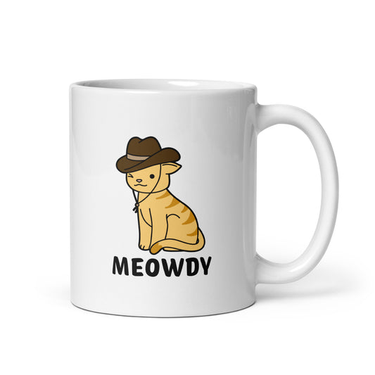 A white, 11 ounce ceramic coffee mug featuring an illustration of an orange striped cat wearing a cowboy hat. The cat is winking and smiling, and text beneath him reads "Meowdy"