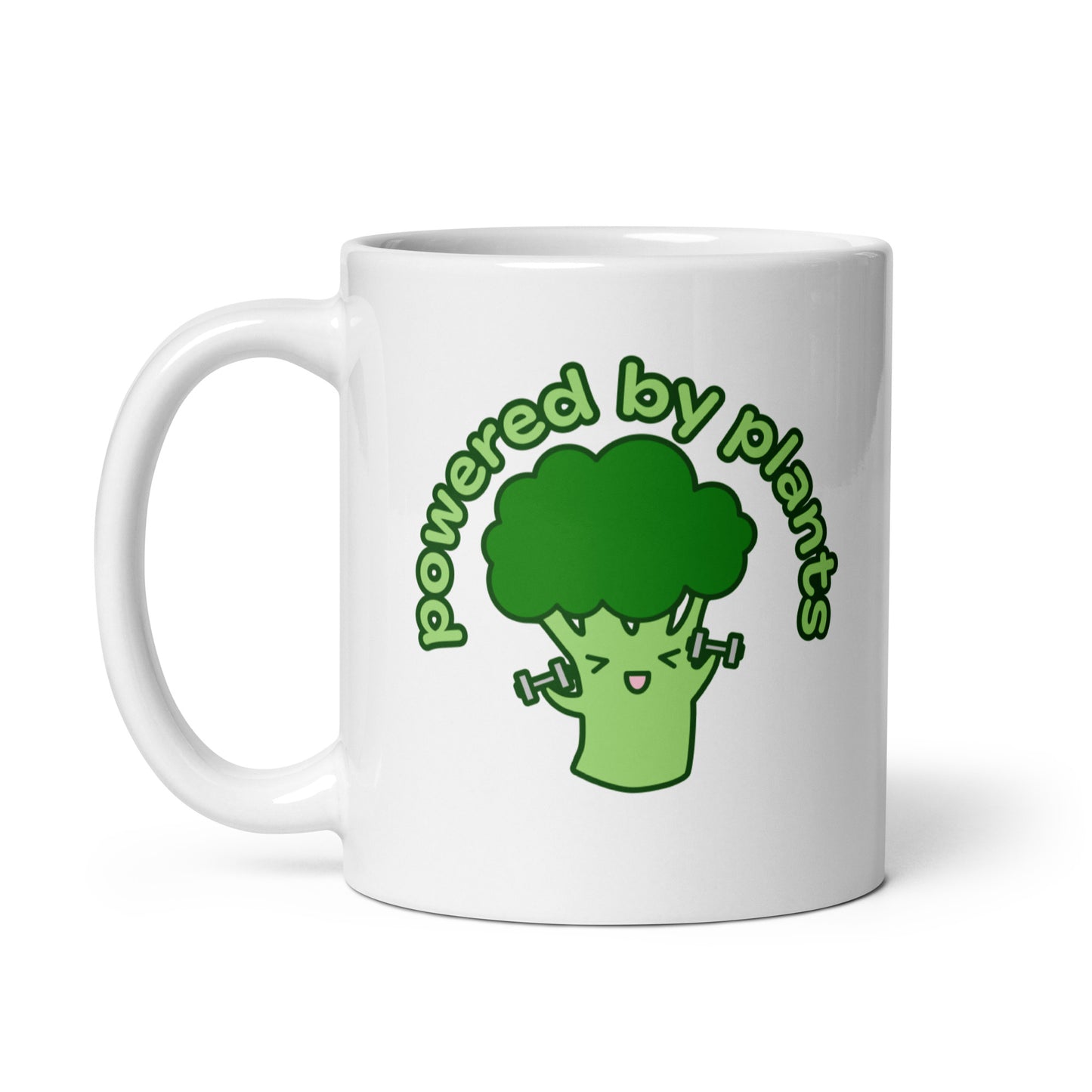A white 11 ounce ceramic coffee mug featuring a cute illustration of a cartoon broccoli. The broccoli is excitedly lifting weights and text above him in an arc reads "powered by plants".