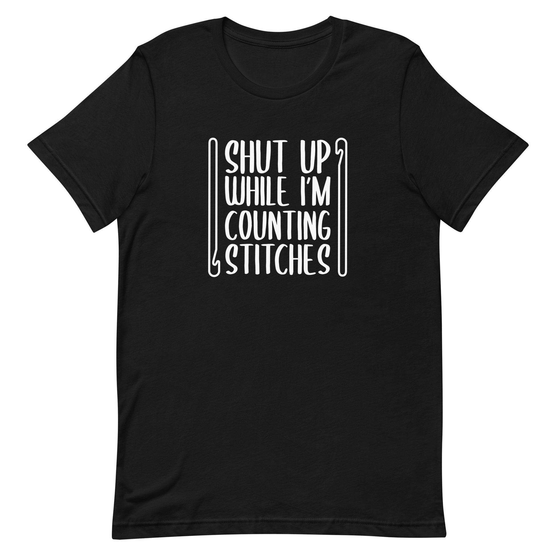 A black crewneck t-shirt featuring white text that reads "Shut up while I'm counting stitches." The text is framed by a crochet hook to the left and right.