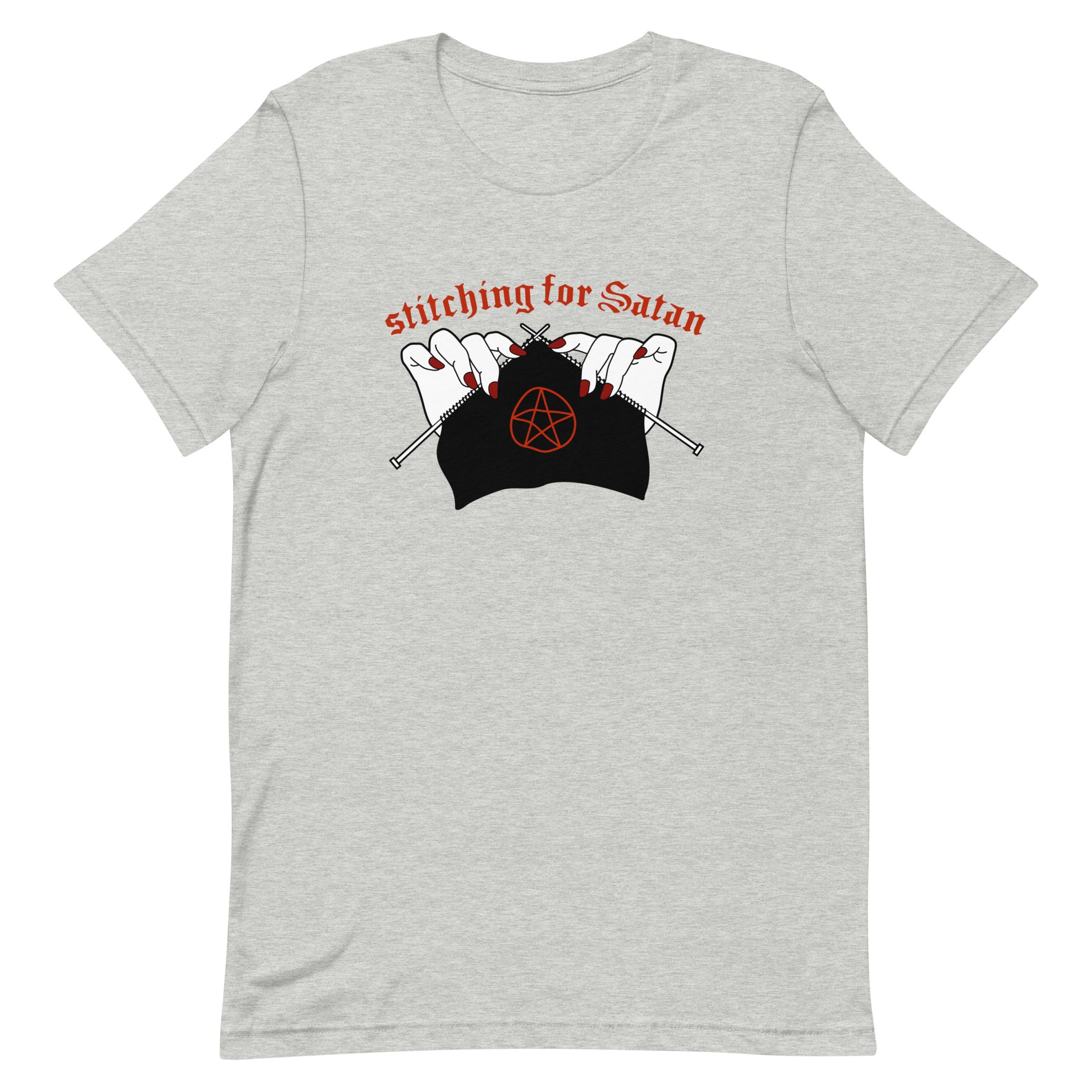 A grey crewneck t-shirt featuring an illustration of pale white hands with red fingernails holding knitting needles. Fabric on the needles features a red pentagram. Text above the hands reads "stitching for Satan" in a gothc red font.