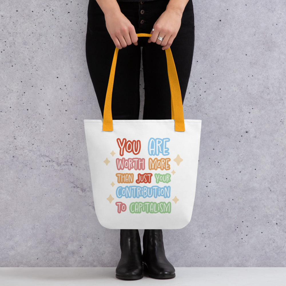 A waist-down image of a person holding white tote bag with yellow handles, featuring colorful hand-written-style text that reads "You are worth more than just your contribution to capitalism". Sparkles surround the text on each side.