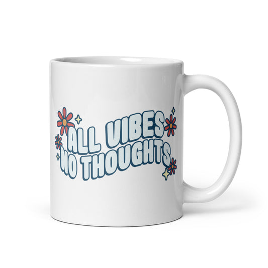 A white ceramic coffee mug featuring text that reads "All vibes no thoughts". Around the text are pink flowers and pale yellow sparkles.
