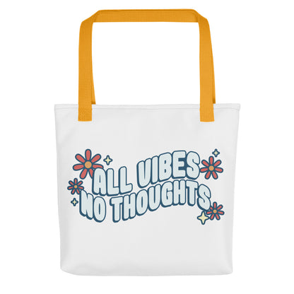 A white tote bag with yellow handles. On the tote bag is text that reads "al vibes no thoughts" with flowers and sparkles.