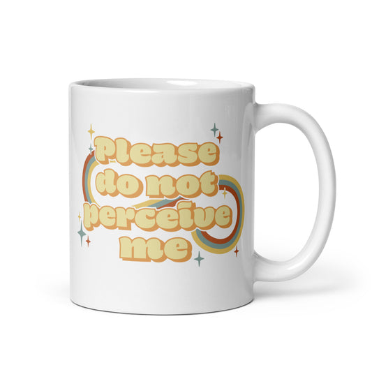 An 11 ounce white ceramic mug featuring vintage-style text that reads "Please do not perceive me". A colorful swirl and sparkles surrounds the text in red, yellow, and blue.