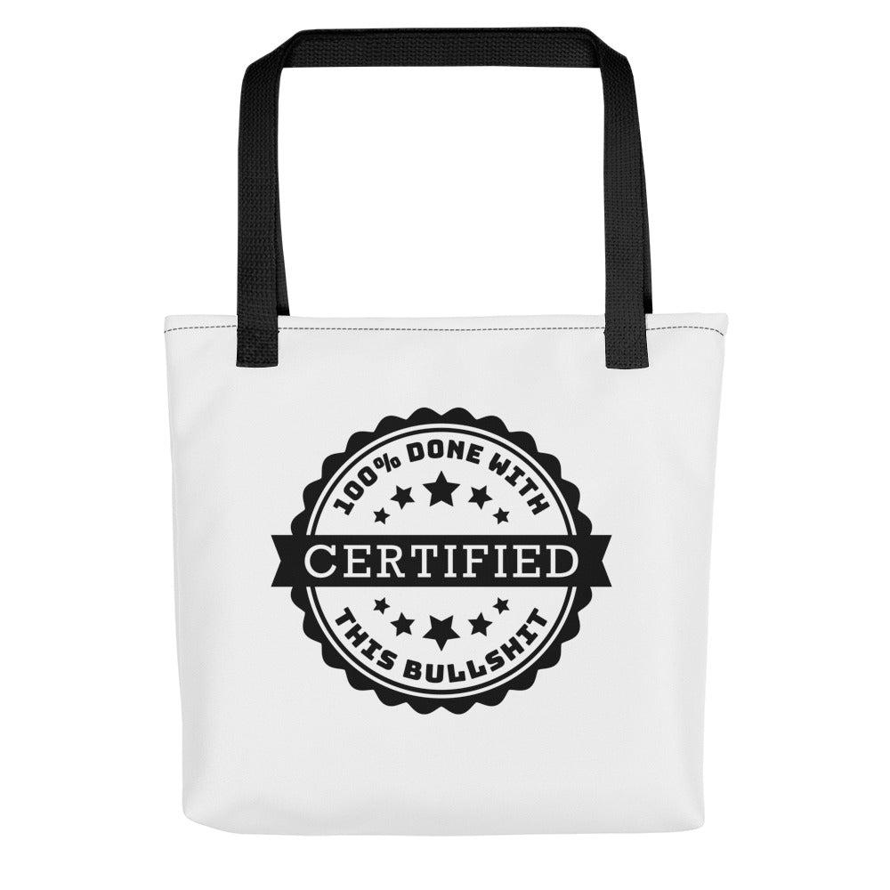 A white tote bag with black handles and stitching. Centered on the bag is an image of an official-looking stamped seal that reads "CERTIFIED: 100% done with this bullshit."
