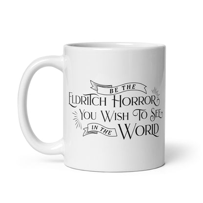 A white, ceramic, 11 ounce mug featuring black text in a semi-gothic style font that reads "Be the Eldritch Horror You Wish To See In The World"