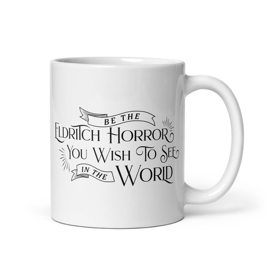 A white, ceramic, 11 ounce mug featuring black text in a semi-gothic style font that reads "Be the Eldritch Horror You Wish To See In The World"