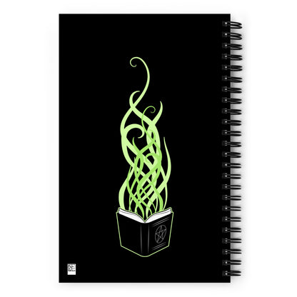 The back of a black wire-bound notebook featuring an illustration of an open spellbook. Green tendrils of magic reach upward from the spellbook's open pages.