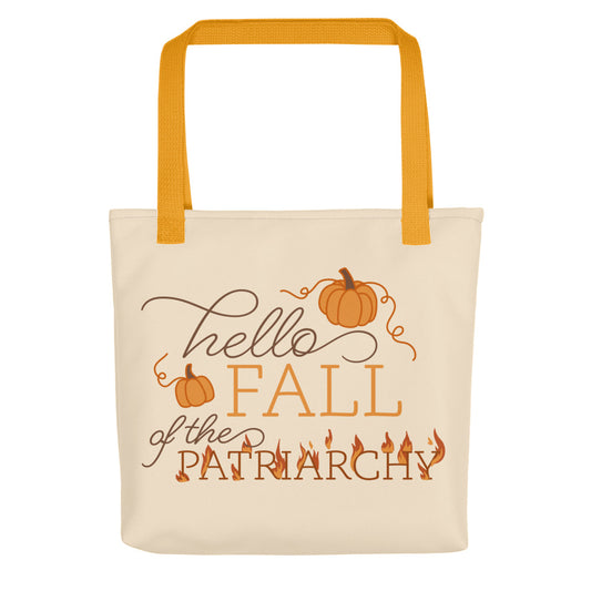A cream-colored tote bag featuring text in a blend of cursive and serif fonts that read "hello FALL of the PATRIARCHY". Pumpkins surround the upper half of the text, and the word "Patriarchy" is surrounded by flames.