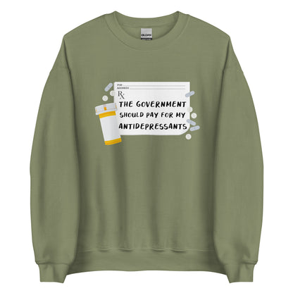 An olive green crewneck sweatshirt featuring an image of a subscription page with text that reads "The government should pay for my antidepressants". Pills and an empty orange pill bottle surround the RX sheet.