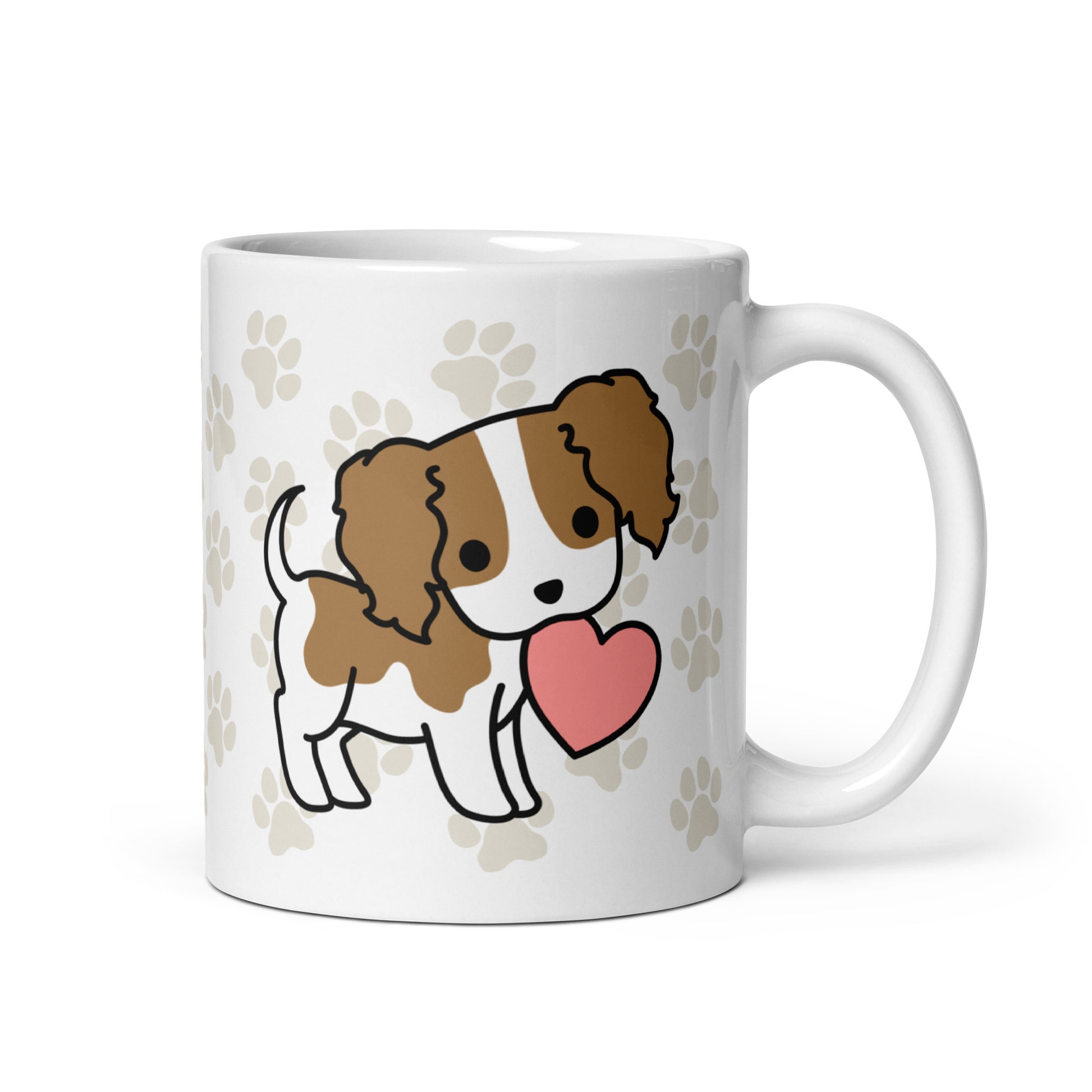 A white 11 ounce ceramic mug with a pattern of light brown pawprints all over. The mug also features a stylized illustration of a Cavalier King Charles Spaniel holding a heart in its mouth.