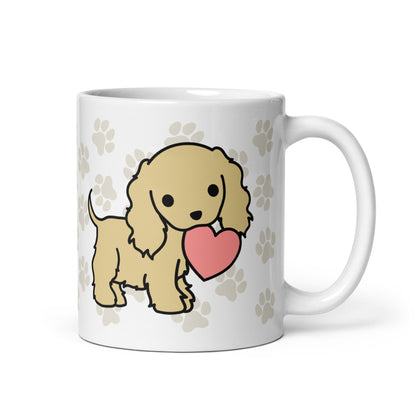 A white 11 ounce ceramic mug with a pattern of light brown pawprints all over. The mug also features a stylized illustration of a Cocker Spaniel holding a heart in its mouth.