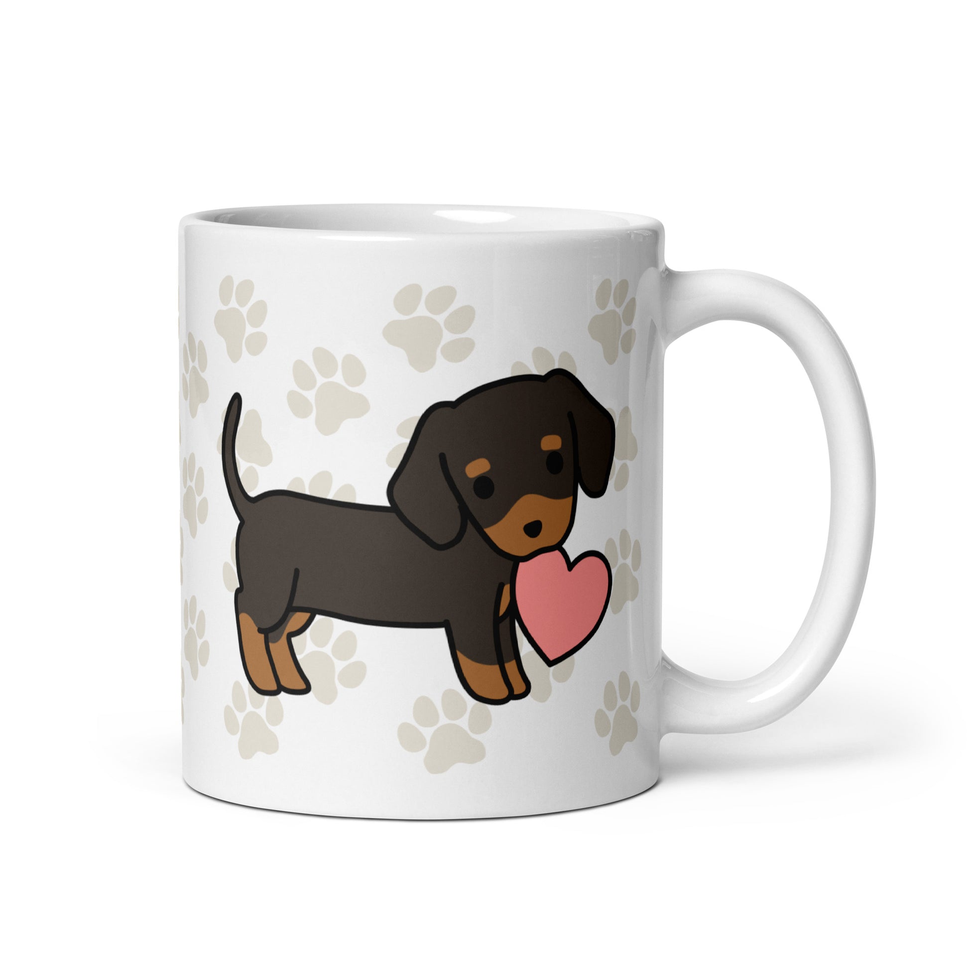 A white 11 ounce ceramic mug with a pattern of light brown pawprints all over. The mug also features a stylized illustration of a Dachshund holding a heart in its mouth.