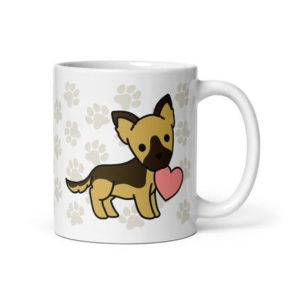 A white 11 ounce ceramic mug with a pattern of light brown pawprints all over. The mug also features a stylized illustration of a German Shepherd holding a heart in its mouth.