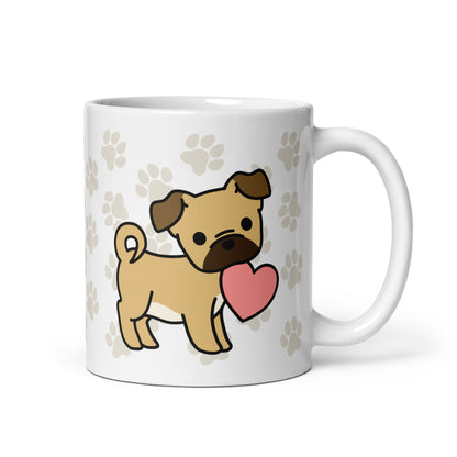 A white 11 ounce ceramic mug with a pattern of light brown pawprints all over. The mug also features a stylized illustration of a Puggle holding a heart in its mouth.