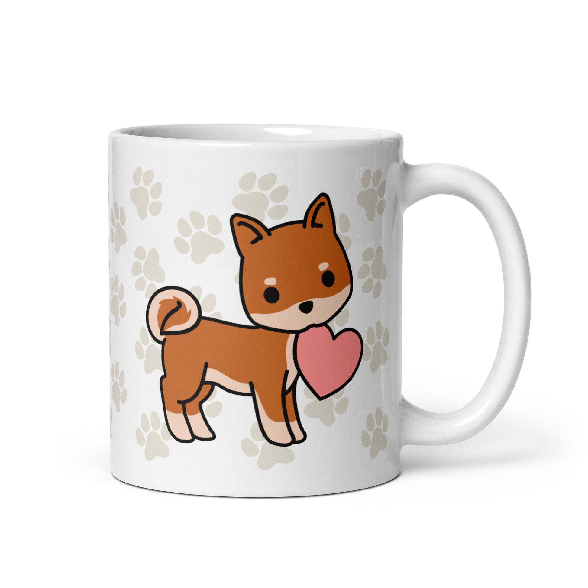 A white 11 ounce ceramic mug with a pattern of light brown pawprints all over. The mug also features a stylized illustration of a Shiba Inu holding a heart in its mouth.