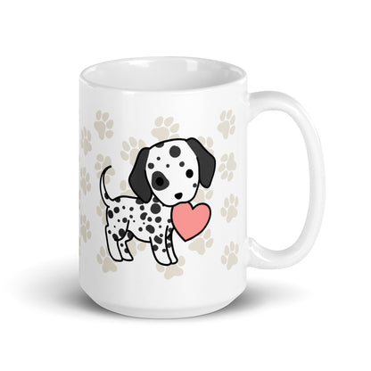 A white 15 ounce ceramic mug with a pattern of light brown pawprints all over. The mug also features a stylized illustration of a Dalmatian holding a heart in its mouth.