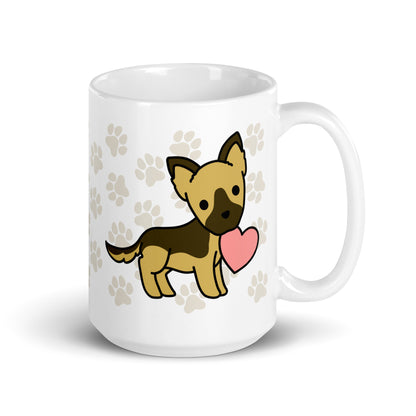 A white 15 ounce ceramic mug with a pattern of light brown pawprints all over. The mug also features a stylized illustration of a German Shepherd holding a heart in its mouth.