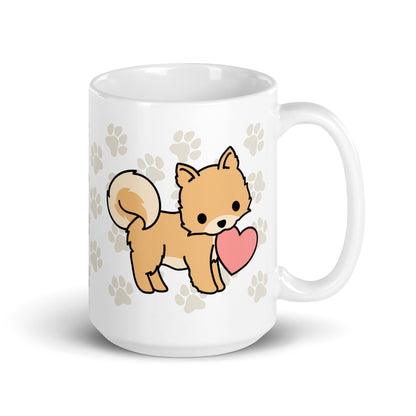 A white 15 ounce ceramic mug with a pattern of light brown pawprints all over. The mug also features a stylized illustration of a Pomeranian holding a heart in its mouth.