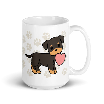A white 15 ounce ceramic mug with a pattern of light brown pawprints all over. The mug also features a stylized illustration of a Rottweiler holding a heart in its mouth.