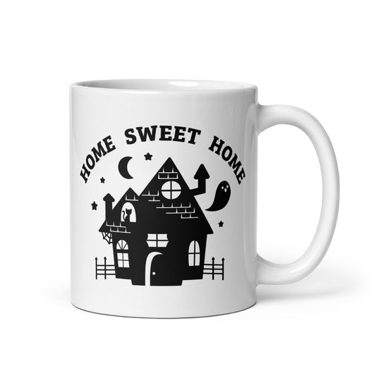 A white 11 ounce ceramic coffee mug featuring an illustration of a haunted house. Text above the house in an arc reads "Home Sweet Home"