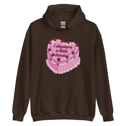 A dark brown hooded sweatshirt featuring an illustration of an elaborately decorated pink cake. Icing on the cake reads "i deserve a little treat" in a cursive font.