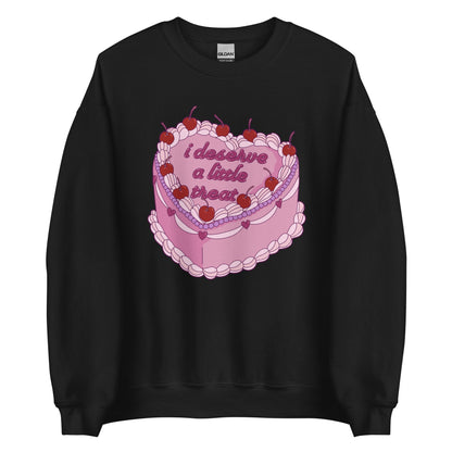 A black crewneck sweatshirt featuring an illustration of an elaborately decorated pink cake. Icing on the cake reads "i deserve a little treat" in a cursive font.