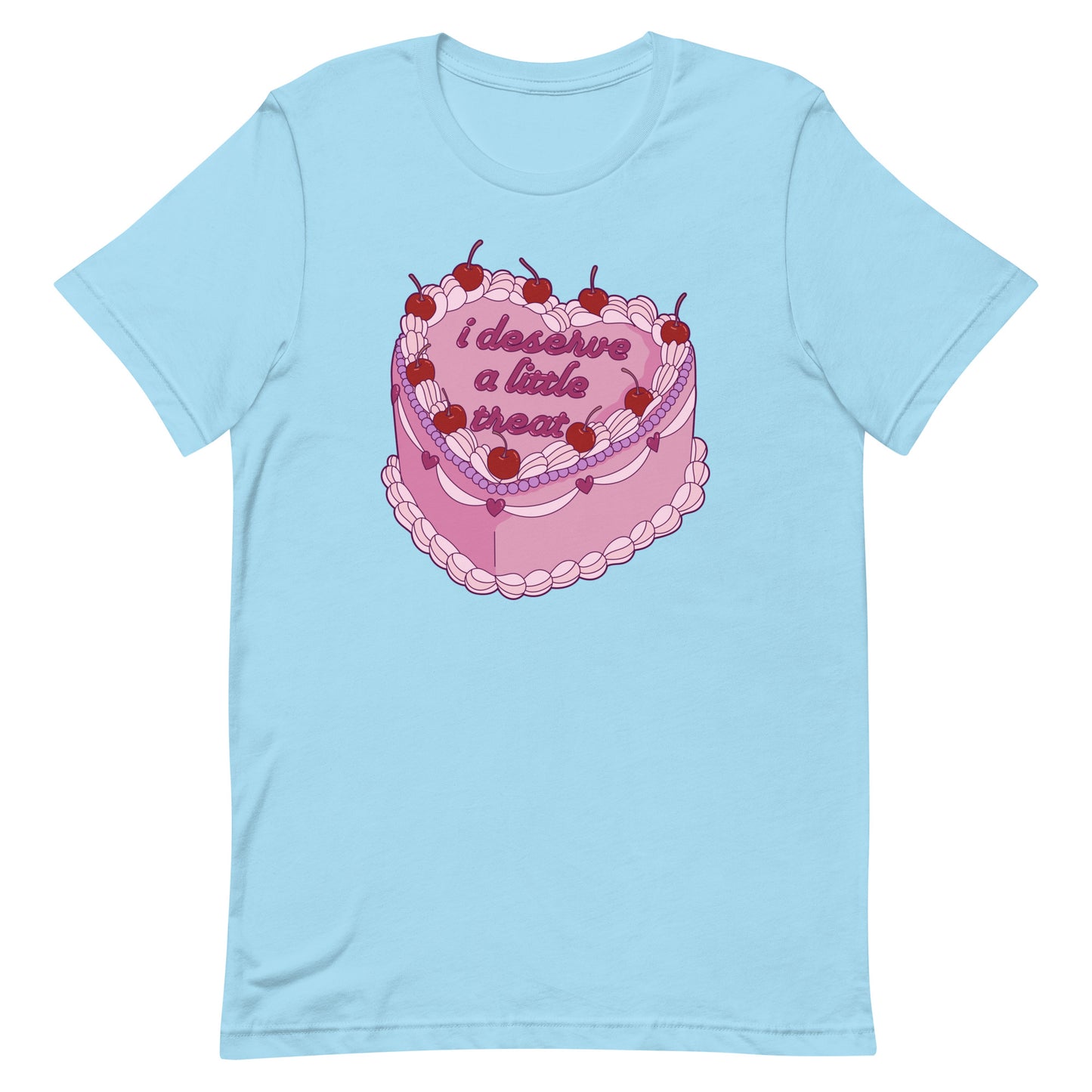 A light blue crewneck t-shirt featuring an illustration of an elaborately decorated pink cake. Icing on the cake reads "i deserve a little treat" in a cursive font.