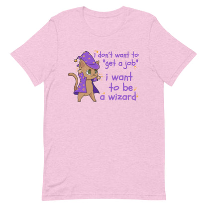 A light pink t-shirt featuring an illustration of a small brown cat wearing a wizard's hat and robes. Scribbly text next to the cat reads "i don't want to "get a job". i want to be a wizard".