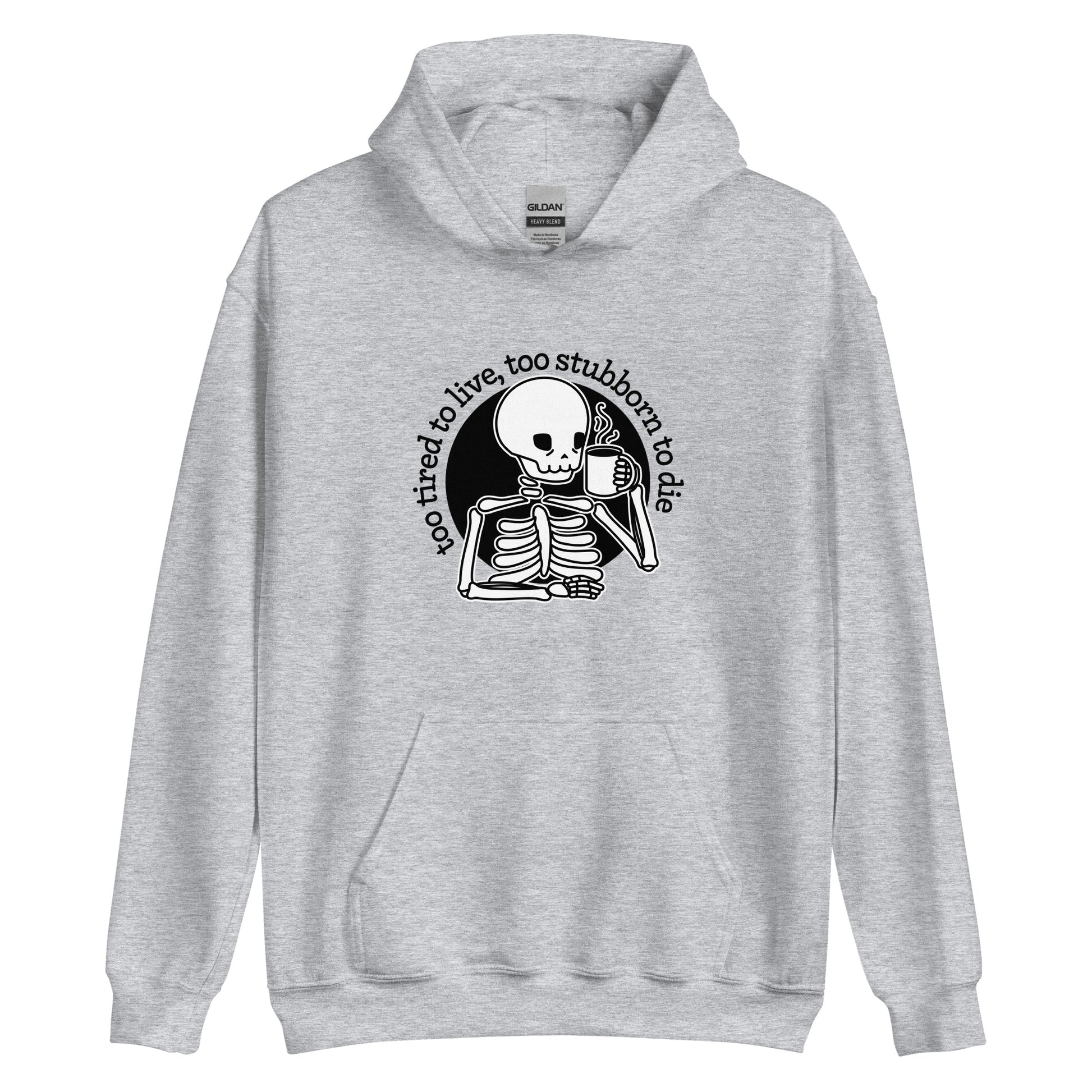 A grey hooded sweatshirt featuring an illustration of a tired-looking skeleton holding a steaming mug. Text in an arc above the skeleton reads "too tired to live, too stubborn to die"