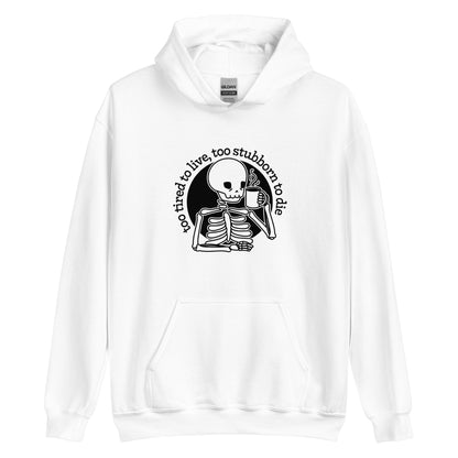 A white hooded sweatshirt featuring an illustration of a tired-looking skeleton holding a steaming mug. Text in an arc above the skeleton reads "too tired to live, too stubborn to die"