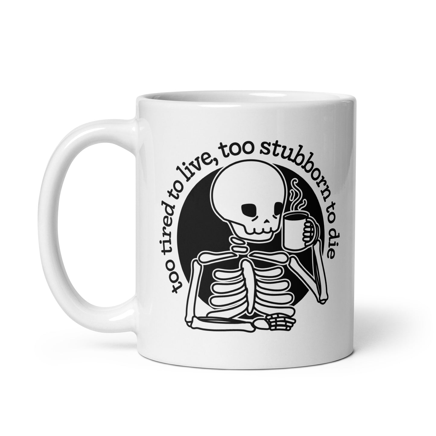 A white 11 ounce ceramic mug featuring a tired-looking skeleton holding a steaming mug. Text above the skeleton reads "too tired to live, too stubborn to die".