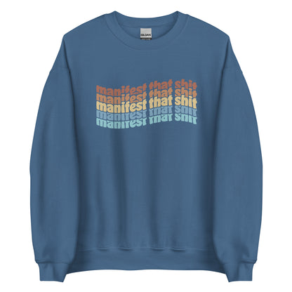 A blue crewneck sweatshirt featuring stacked text that reads "manifest that shit" in a rainbow of colors.