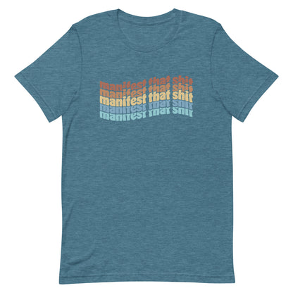 A heathered teal crewneck t-shirt featuring stacked text that reads "manifest that shit" in a rainbow of colors.