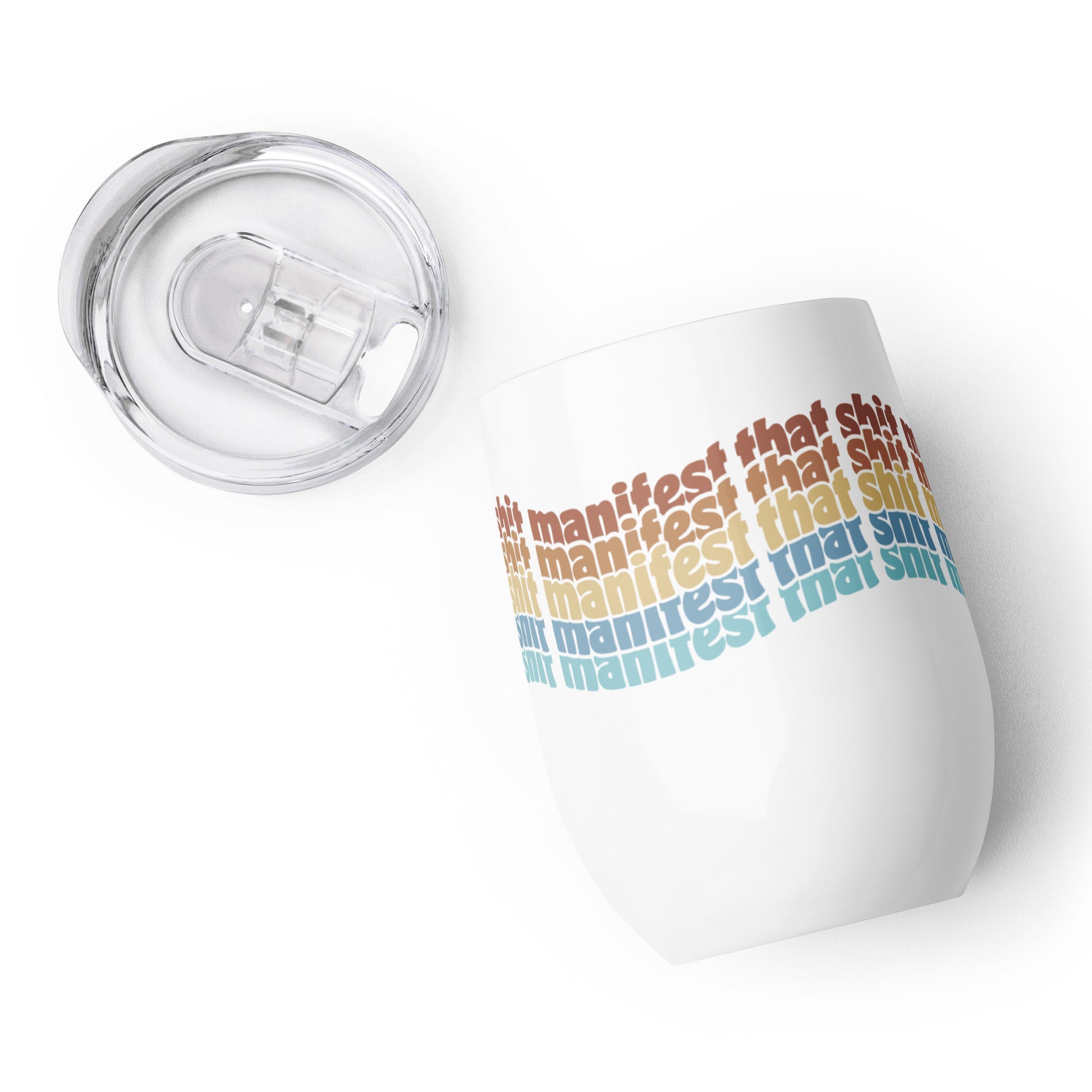 A close-up image of a wine tumbler, laying open on its side. The tumbler's plastic lid is laying next to the tumbler. Rainbow text wraps around the tumbler that reads "manifest that shit".
