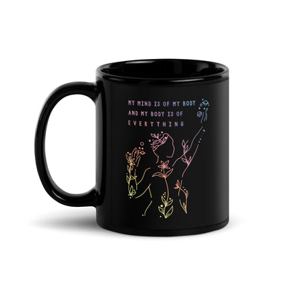 A black 11 ounce coffee mug featuring an abstract illustration of a figure whose body is spreading out into plants and planets and stars. Text above the figure reads "My mind is of my body and my body is of everything."