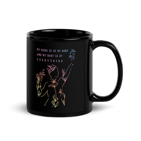 A black 11 ounce coffee mug featuring an abstract illustration of a figure whose body is spreading out into plants and planets and stars. Text above the figure reads "My mind is of my body and my body is of everything."