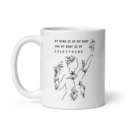 A  white 11 ounce coffee mug featuring an abstract illustration of a figure whose body is spreading out into plants and planets and stars. Text above the figure reads "My mind is of my body and my body is of everything."