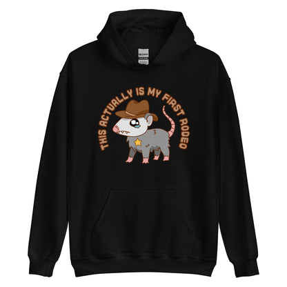 A black hooded sweatshirt featuring an illustration of a cute and nervous possum wearing a cowboy hat and sherrif's star badge. Text above the possum in an arc reads "this actually is my first rodeo".